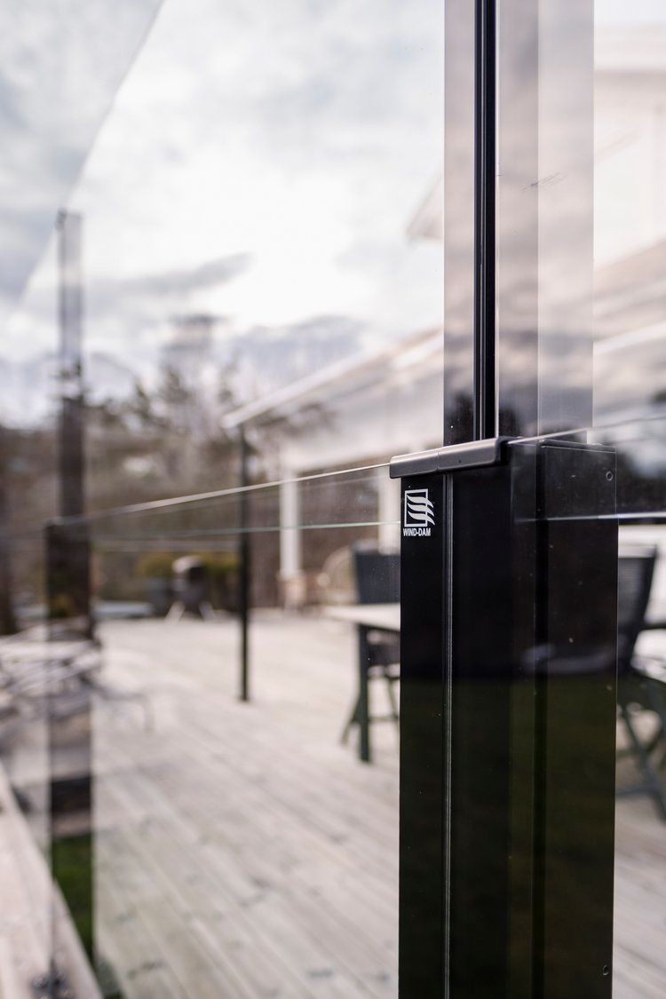 Close-up view of a glass windbreak on an outdoor deck with reflections of trees and sky.